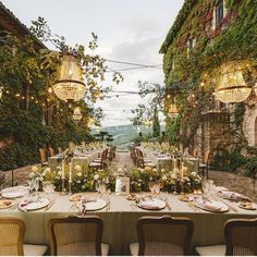 an outdoor dining area with tables and chairs set for dinner, surrounded by greenery