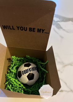 a soccer ball in a box that says, will you be my godfatner?