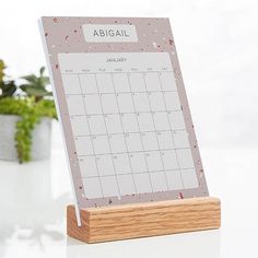 a desk calendar on a wooden stand next to some potted plants in the background