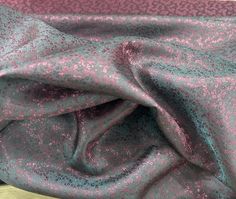 a pink and blue fabric with small speckles on the top, laying on a bed