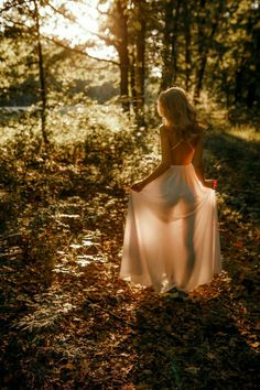 a woman in a white dress is walking through the woods with her back to the camera