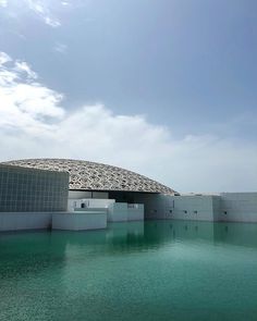 a large building sitting on top of a body of water next to a white wall