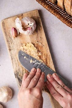 a person is cutting up some food on a wooden board next to garlic and bread