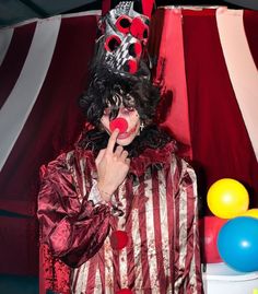 a clown wearing a red and white striped suit with balloons around his head, making a funny face