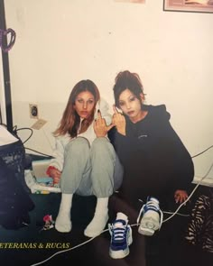 two young women sitting on the floor in front of a wall