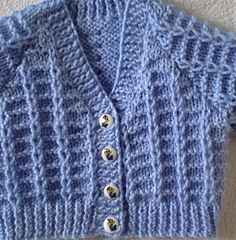 a blue knitted cardigan with buttons on the front and back, sitting on a white carpet