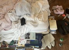 an unmade bed with clothes, books and other items on the floor next to it