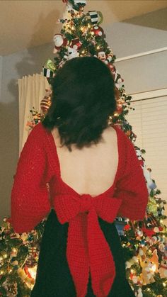 a woman standing in front of a christmas tree wearing a red sweater and black skirt