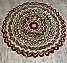 a crocheted round rug with red and green accents on a wooden floor in front of a white wall