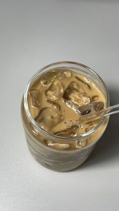 a glass jar filled with liquid sitting on top of a white table next to a spoon