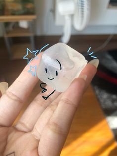 a person's hand holding a small plastic object with a face drawn on it