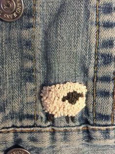 there is a small sheep in the pocket of a jean jacket with buttons on it