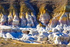 many different colored rock formations in the desert with snow on them and grass growing all around