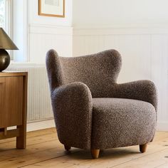 a brown chair sitting on top of a hard wood floor next to a table and lamp