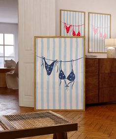 three framed pictures hang on a clothes line in a room with wood floors and wooden furniture