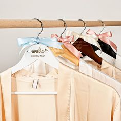 three different colored shirts hanging on a wooden hanger with ribbons attached to them,