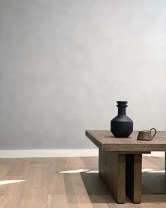 a black vase sitting on top of a wooden table next to a brown coffee cup