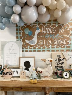 a table topped with balloons and pictures next to a sign that says have is one silly goose