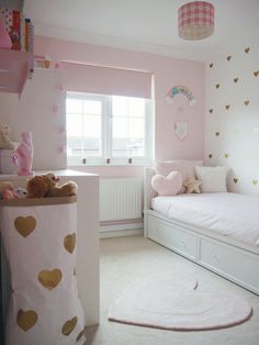 a child's bedroom with pink walls and gold hearts on the wall, white bedding