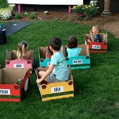 several children are sitting in cardboard cars on the grass