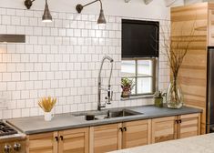 a kitchen with wooden cabinets and white tile backsplash, black roller shades over the window