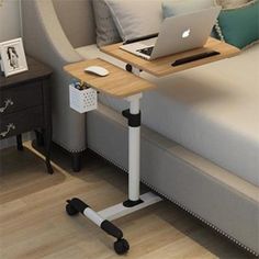 a laptop computer sitting on top of a wooden table next to a bed with white pillows