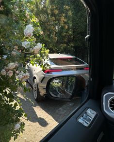 the rear view mirror of a car parked in front of a tree with white flowers