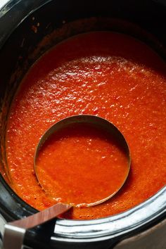 a wooden spoon in a slow cooker filled with tomato sauce, ready to be cooked