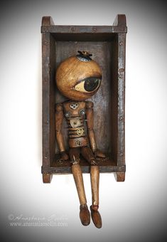 a wooden doll sitting in a box with its eyes closed and hands on her hips