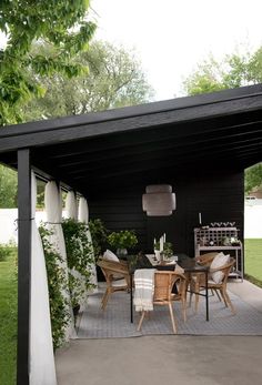 an outdoor dining area with table and chairs under a covered patio, surrounded by greenery