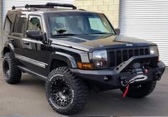 a black jeep parked in front of a garage door with its lights on and the hood off