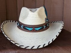 The Maverick starts with a Mexican soft palm leaf hat body that has a 3 3/4" brim and 5 1/4" crown. Hand laced in chocolate brown leather lace. The beaded hatband has a Thunderbird pattern and then mounted on distressed leather. The back of the band has a deer antler bead for accent. Starburst turquoise Concho and deep blue/green decorative feather completes the hat. All hats are made to order. Allow up to 4 weeks for your hat to ship. Brown Toquilla Straw Hat Bands For Ranch, Western Style Brown Panama Hat With Flat Crown, Brown Toquilla Straw Hat Band For Western-themed Events, Western Brown Panama Hat With Flat Crown, Handmade Brown Straw Hat For Kentucky Derby, Custom Curved Brim Straw Hat For Rodeo, Artisan Brimmed Straw Hat For Rodeo, Brown High Crown Country Hat, Traditional Handmade Hats For Western Events