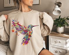 "Hummingbird Sweatshirt, Gift For Her, Spring Birds, Bird Sweatshirt, Bird Lover Gift, Watercolor Hummingbird, Floral Hummingbird Shirt Matching T-Shirt: https://www.etsy.com/PrintWorkShopCompany/listing/1504229365/floral-hummingbird-shirt-animal-lover?utm_source=Copy&utm_medium=ListingManager&utm_campaign=Share&utm_term=so.lmsm&share_time=1688570829048 ** HOW TO ORDER 1. Check our photos for sizing and color options.  2. Select your size and color from the drop-down menus.  3. Click \"ADD TO CA Spring Wardrobe Essentials, Nature Inspired Fashion, Watercolor Hummingbird, New York Sweatshirt, Floral Sweatshirt, Holiday Hoodies, Design Sweatshirt, Sweatshirt Graphic, California Girl