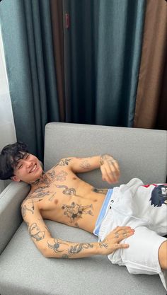 a man laying on top of a couch with tattoos on his chest and arms,