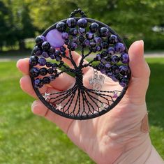 a person holding up a brooch with beads on it's face and tree of life in the middle