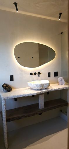 a white sink sitting under a mirror next to a wooden shelf with lights on it