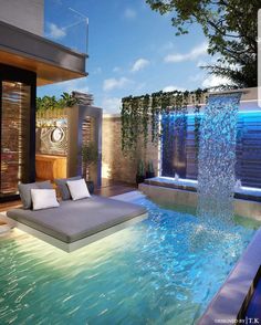 an outdoor swimming pool with waterfall and lounge chair next to it in the evening time