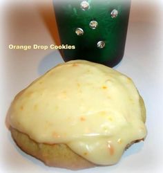 an orange drop cookies with white icing next to a green cup