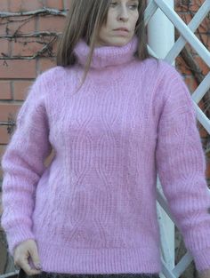 a woman standing next to a brick wall wearing a pink sweater