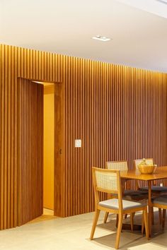 a dining table and chairs in front of a wooden wall with vertical slats on it