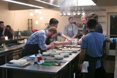 a group of people standing around a kitchen preparing food on top of a countertop