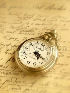 a pocket watch sitting on top of an old sheet of paper with writing in the background