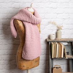 a mannequin with a pink knitted scarf on it's head next to a white brick wall