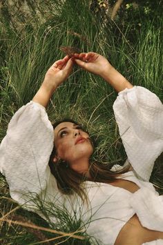 a woman laying in the grass with her hands on her head and eyes closed, looking up