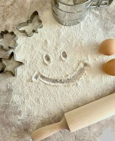 a smiley face made out of flour next to two cookie cutters and an egg