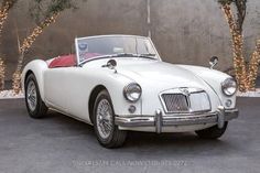 an old fashioned white car parked in front of a wall with christmas lights on it