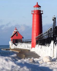 a red light house sitting on top of a snow covered pier next to the ocean