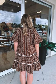 Living out our Southern Chic daydreams in this tiered mini dress. Gorgeous, puff-sleeve, design and a boho inspired floral pattern. Notch, v-neckline with a ruched collar. This dress features hidden side pockets and a built-in lining. Tie straps in the front with a gold metal detail at the ends. Emmy is seen wearing a size medium. Self: 100% cotton Contrast: 80% polyester, 20% cotton Lining: 100% polyester