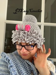 a woman wearing a crocheted hat with pink flowers on it and holding her hand up to her ear