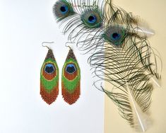 two peacock feathers are next to a pair of beaded earrings on a white surface